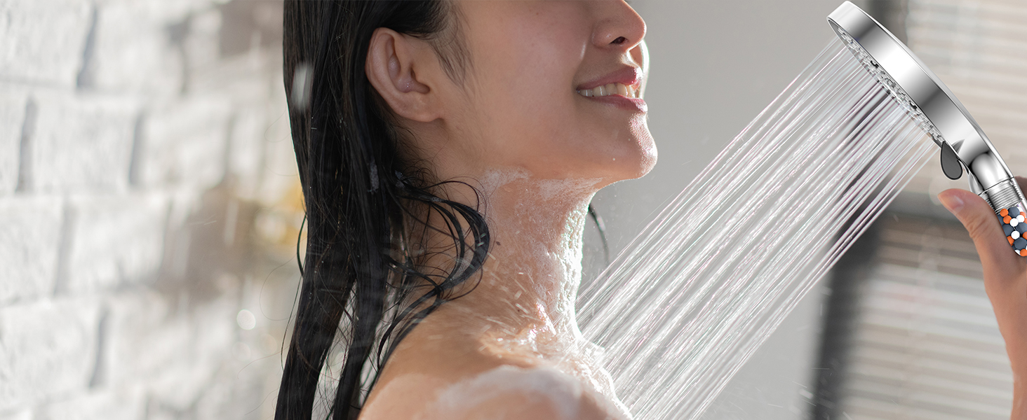 avec plusieurs jets d'eau pulvérisés sur le cou et les épaules d'une personne. Luminaire chromé visible sur fond carrelé blanc