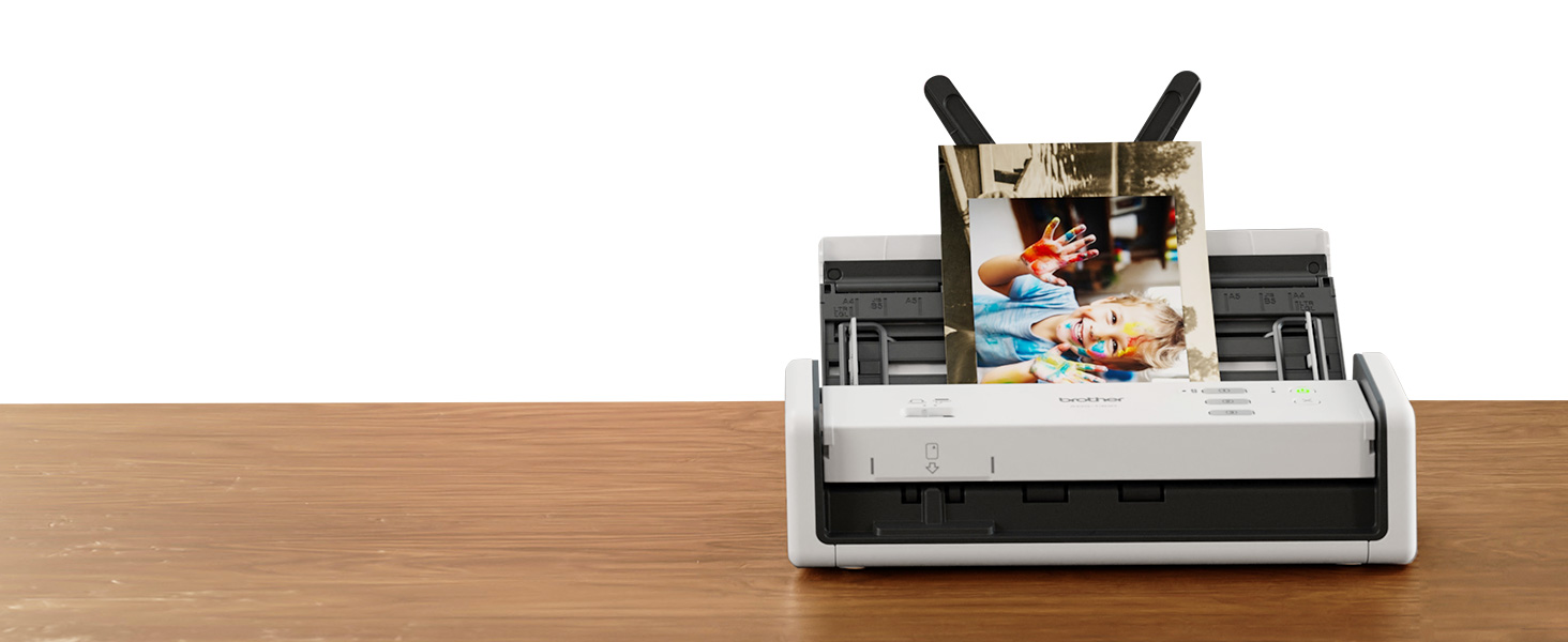 Brother ADS1300 white and grey compact scanner on desk, with 4" x 6" family photos in document feed