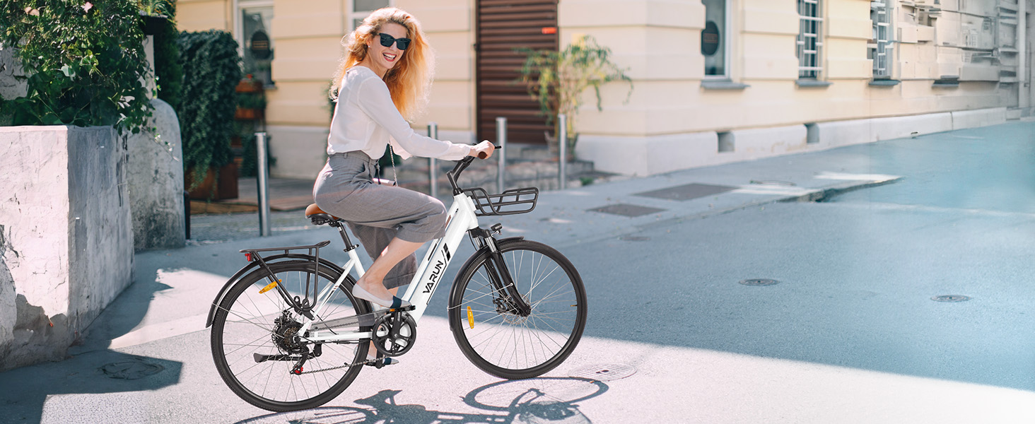 Weißes Elektrofahrrad mit hinterem Gepäckträger, das auf einer städtischen Straße gefahren wird. Es verfügt über ein modernes Rahmendesign und eine integrierte Batterie.