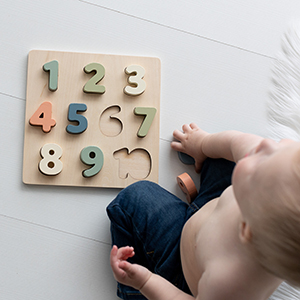 Young child playing with wooden number puzzle in playroom