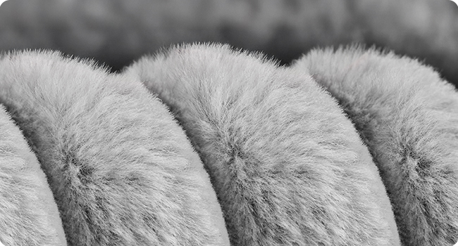 Nahaufnahme in Schwarz-Weiß, die flauschiges oder pelziges Textilmaterial in verschiedenen Stadien der Kompression oder Manipulation zeigt.