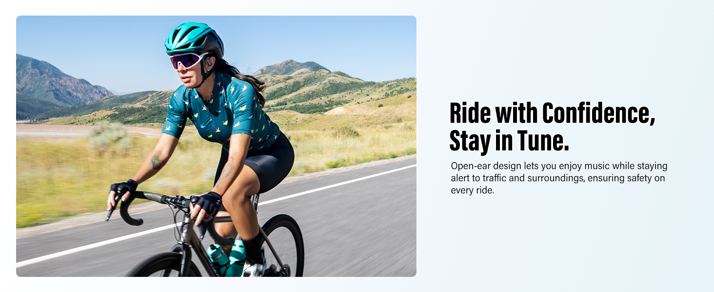 Cyclist wearing teal cycling gear and helmet riding a road bike on a paved road with mountains and grasslands in the background.