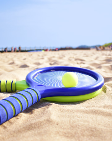 2 plastic boom bats and a pingpong ball in the sand at a sunny beach 