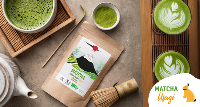 : paquete de té «MATCHA», batidor de bambú, tazas de matcha preparado con latte art. Logotipo de «Matcha Usagi» visible. Bandejas de madera y fondo neutro