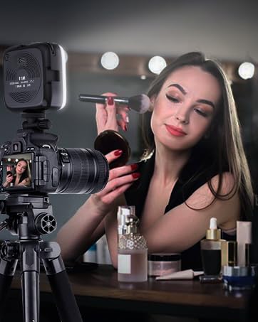 Woman operating professional camera on tripod in well-lit setting with vanity mirror and cosmetics visible in background.