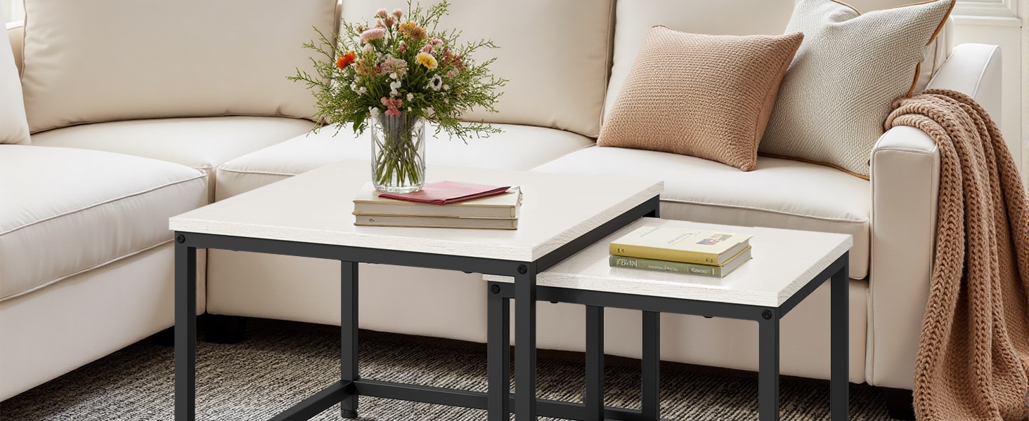 Modern living room setting with white sofa, beige throw pillows, and contemporary coffee tables featuring white tops and black metal frames.