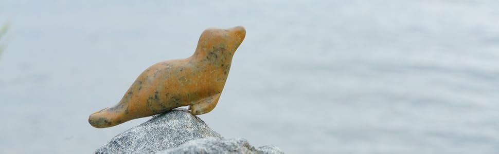 Soapstone seal sculpture on rock by ocean