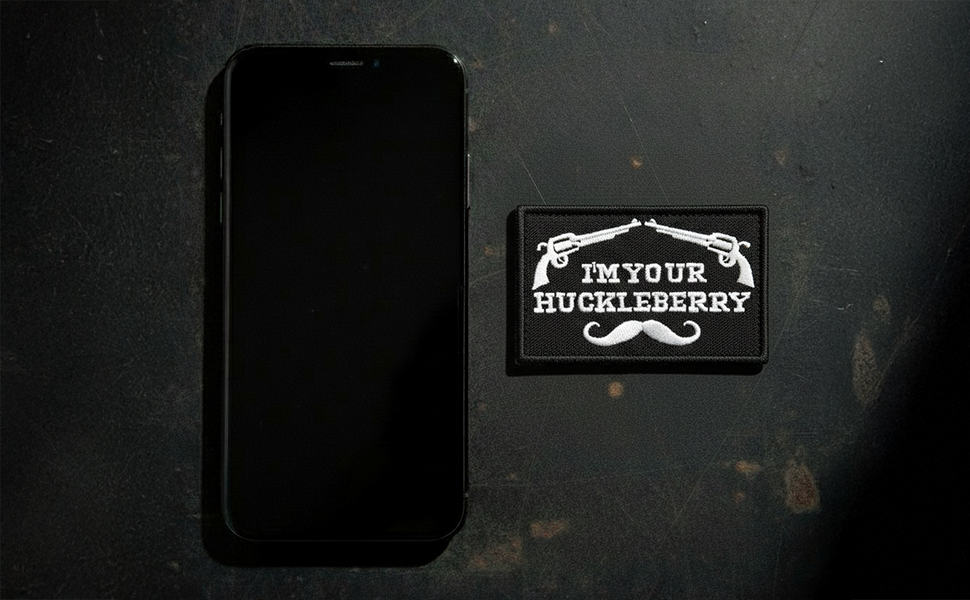 05-A black smartphone lies on a dark textured surface beside a patch with two pistols and the phrase
