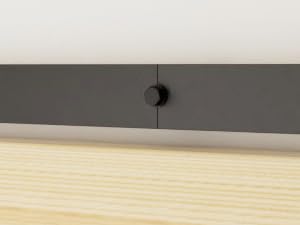 Nahaufnahme eines minimalistischen grauen Möbelstücks mit einem einzigen runden schwarzen Knopf vor einer weißen Oberfläche und hellem Holzboden