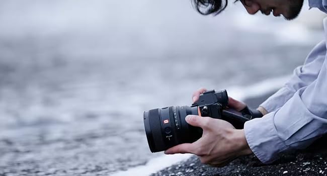 image of a man holding camera at a low angle aimed at waves