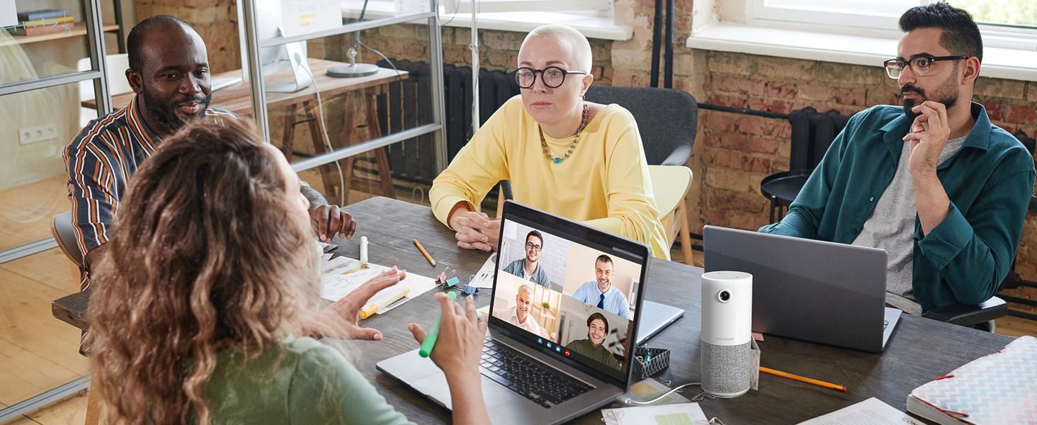 Group video conference with people in office and on laptop screen. White cylindrical smart speaker on table.