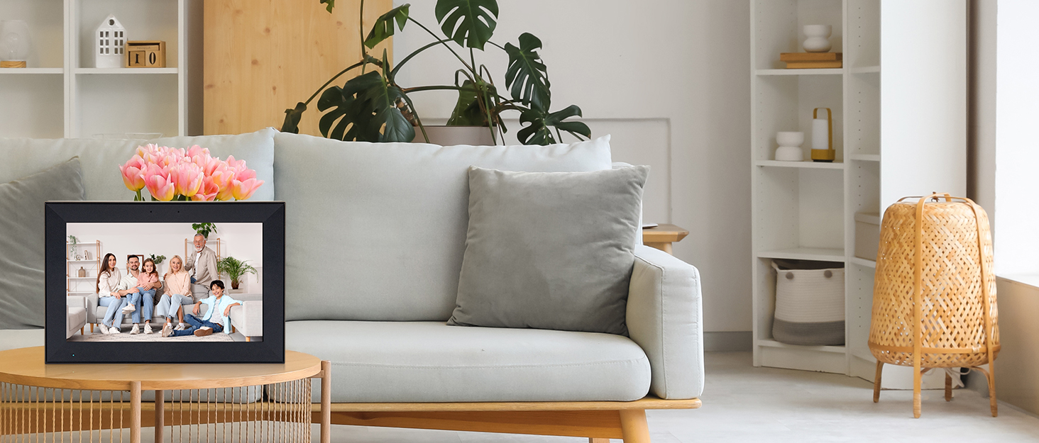 Living room interior with gray sofa, digital photo frame on coffee table, potted plants, and shelving units. Warm, cozy atmosphere.