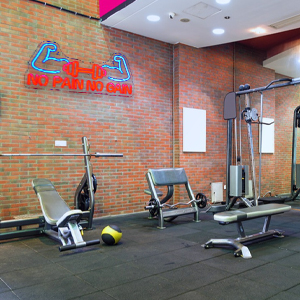 Indoor gym space with exposed brick walls featuring various exercise equipment including weight machines and cardio equipment on rubber flooring.