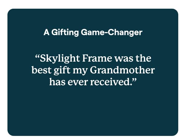 Skylight digital photo frame on table, with hand holding phone.