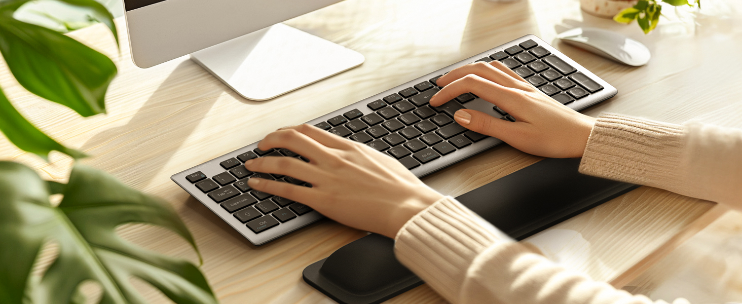 Keyboard wrist rest pad in use on desk with computer setup, showing ergonomic support while typing.