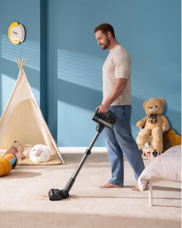 Mann mit Standstaubsauger auf Teppich im Kinderzimmer. Blaue Wände, Tipizelt und Stoffbär