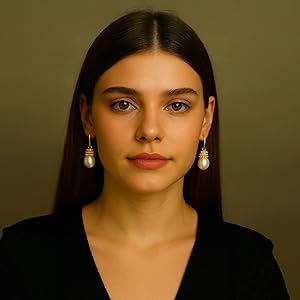 Gold drop earrings featuring a round pearl-like bead suspended from a smaller spherical top. Worn by a model against a dark background.