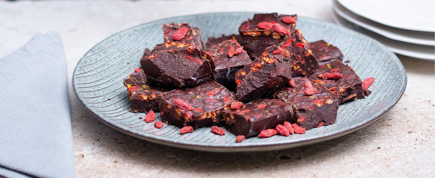 Plate of dark, square-shaped food items with reddish edges, possibly chocolate or fudge pieces, garnished with red flakes or fruit bits.