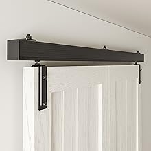 Black wooden barn door hardware track system mounted above a white door, featuring metal brackets and a horizontal rail for sliding functionality.