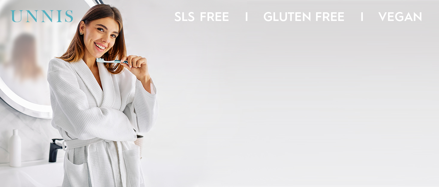 White terry cloth bathrobe worn by a woman. Product is SLS-free, gluten-free, and vegan. Brand name 'UNNIS' visible at top of image.