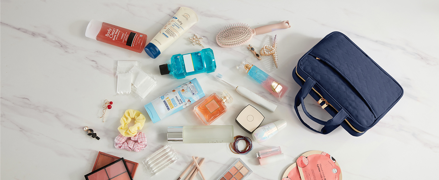 Travel essentials laid out on light background. Items include toiletries, medication, compact mirror, sunglasses, and a navy travel bag.