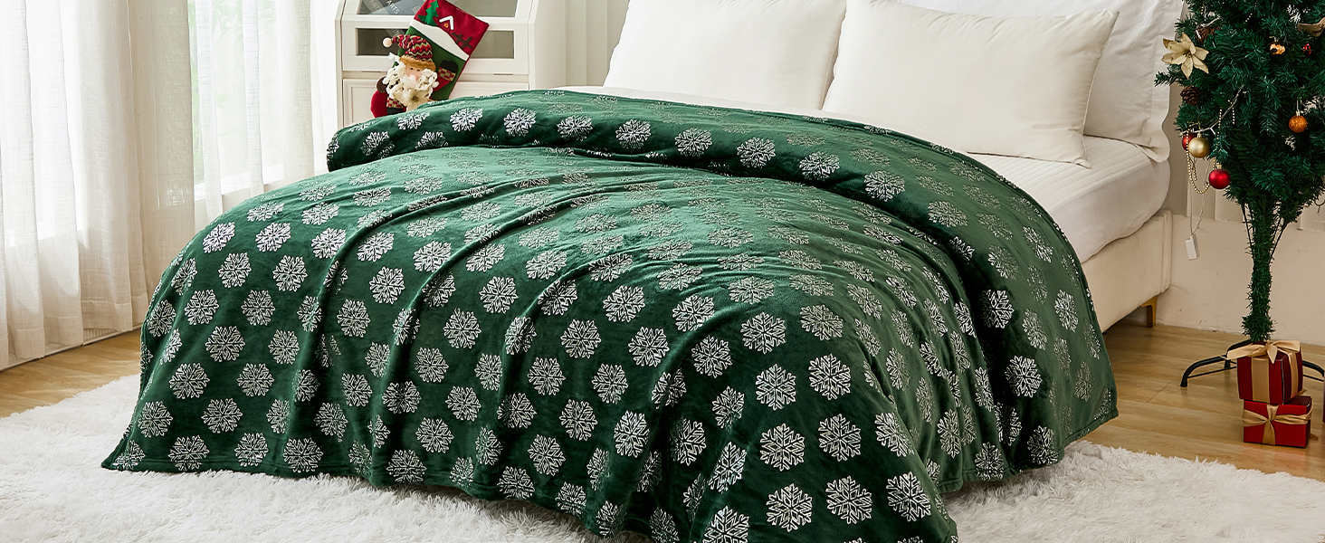 Green bedspread with white floral pattern on a bed in a room with Christmas decorations. Visible tree and gifts in background.