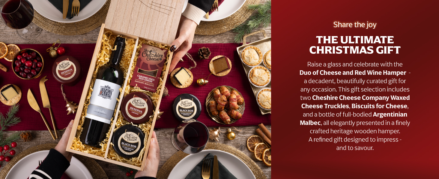 Text reads 'THE ULTIMATE CHRISTMAS GIFT'. Overhead view of wooden gift box containing wine bottle and gourmet items arranged on dark red surface with decorative elements.