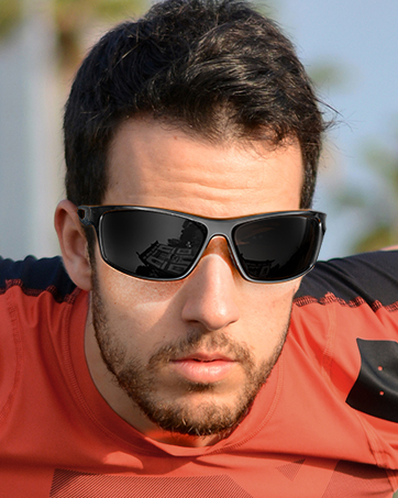 Black sport sunglasses with reflective lenses worn by a person in a red shirt outdoors. Sunglasses have a wraparound style with wide temples for sun protection.
