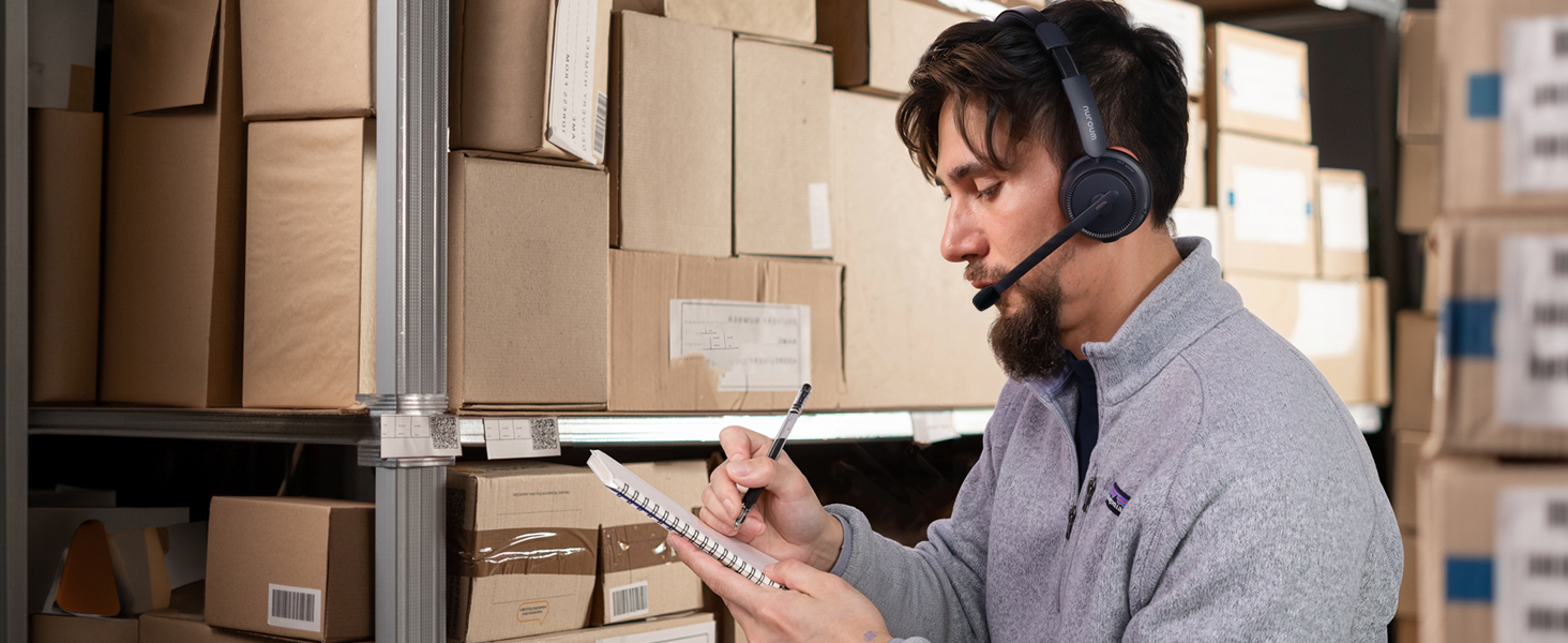 Person scanning boxes in a warehouse setting with handheld device, surrounded by stacked cardboard boxes and storage shelves.