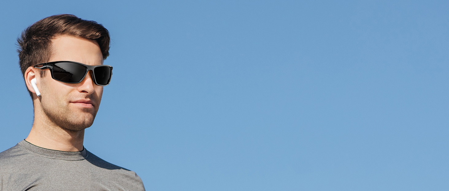 Black sunglasses with thick frames worn by a person against a blue sky background. The sunglasses have a modern, rectangular shape with dark lenses.