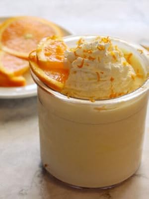 Orange ice cream in a glass, topped with whipped cream, zest, and a fresh orange slice.