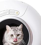 White, spherical pet device with a circular opening. Inside, a gray tabby cat is visible, licking its nose. Warning labels are visible on the top of the device.