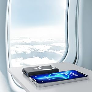 Smartphone displaying glowing blue logo placed on airplane tray table near window, with cloudy sky visible through aircraft window.