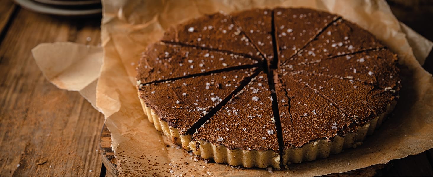 Circular chocolate tart on parchment paper. Tart is sliced into wedges and dusted with powdered sugar, set on a wooden surface.