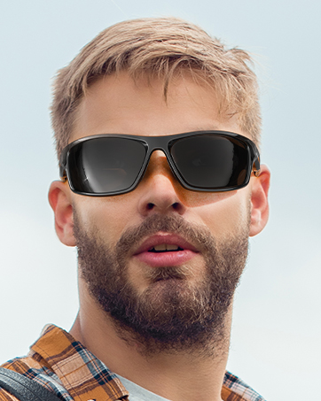 Black wrap-around sunglasses with wide frames and dark lenses, worn by a person with blonde hair and a beard.
