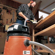 A woodworker uses a shop vacuum connected to a power tool to control dust as he works
