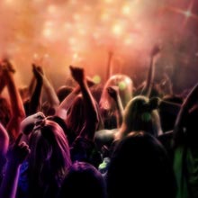Silhouetten von Konzertbesuchern mit erhobenen Händen vor dunklem Hintergrund mit lila und orangefarbener Bühnenbeleuchtung