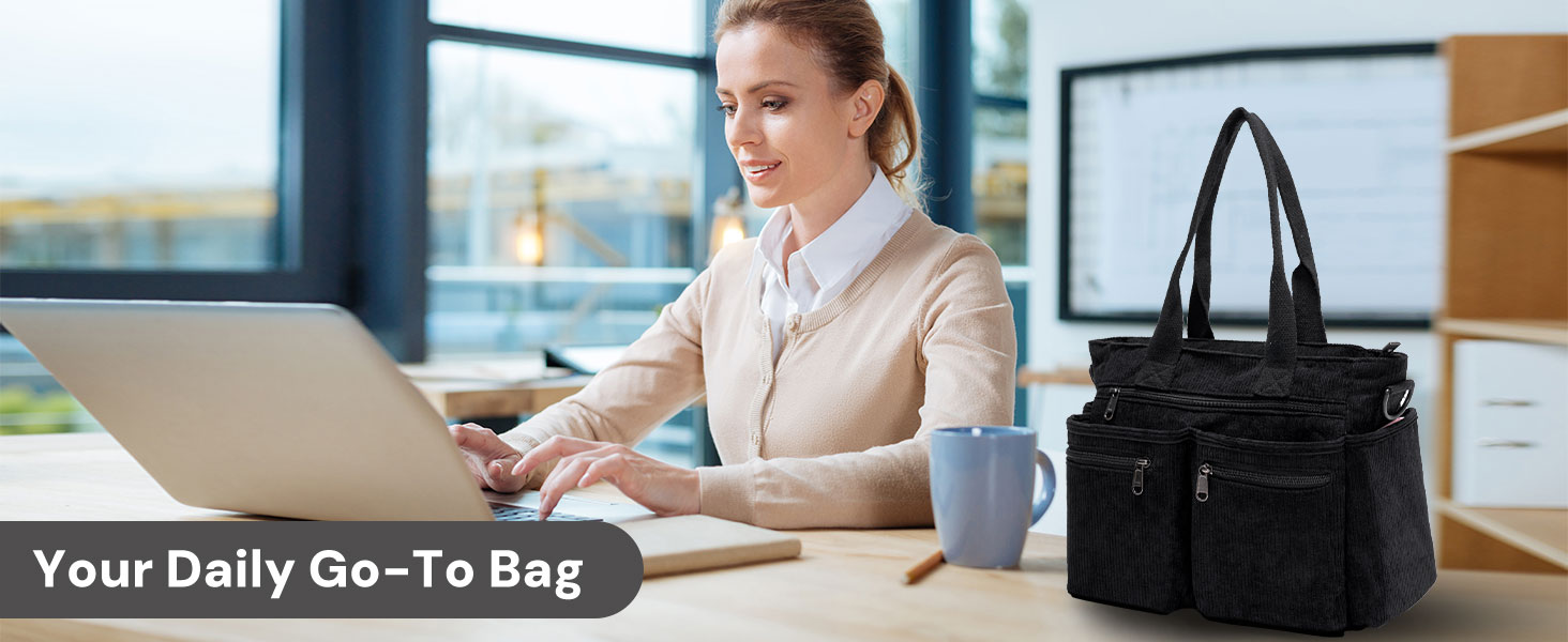 Black tote bag on office desk next to a woman using laptop; ideal for daily work routines