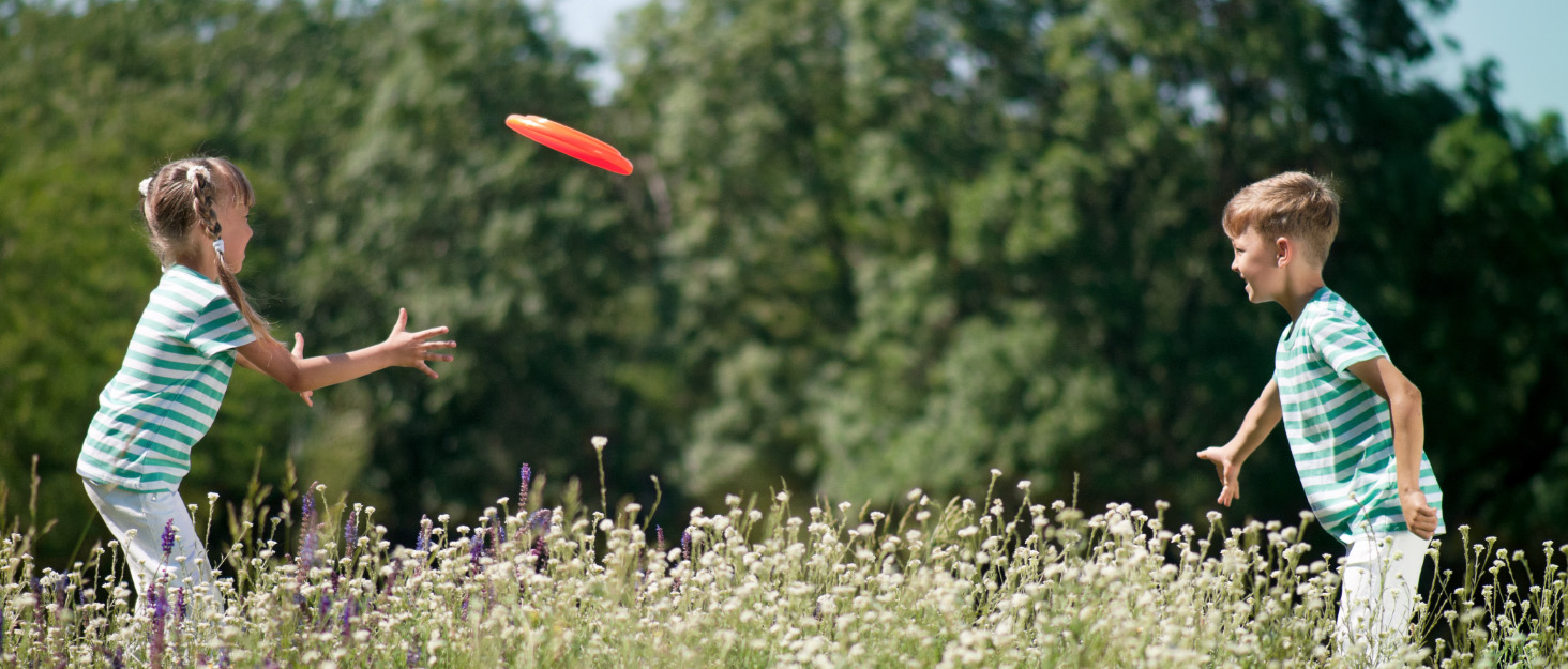 a brother and sister play catch with a Frisbee together