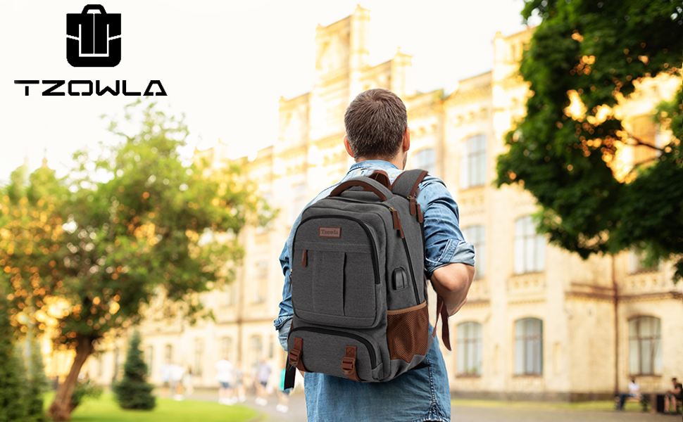 Sac à dos gris foncé aux accents bruns porté par une personne faisant face à un bâtiment historique. Des arbres et de l'herbe sont visibles au premier plan.