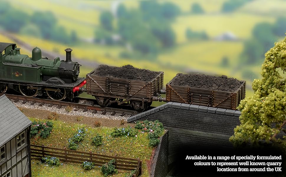 Miniature model train scene with steam locomotive, cargo wagons, and rural landscape including a half-timbered building and fields.
