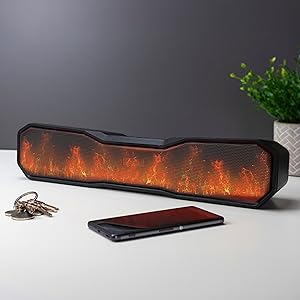 Portable Bluetooth speaker with animated flame effect display, shown next to a smartphone and keys. Black rectangular design with orange LED lights simulating fire.