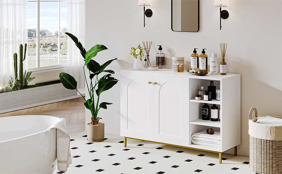 Modern white bathroom cabinet with gold feet, featuring open shelving and closed storage, styled with plants, bottles, and bathroom accessories.