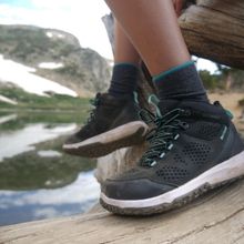 Woman wearing Northside Benton Mid Hiking Boots on a log near water and a mountain.