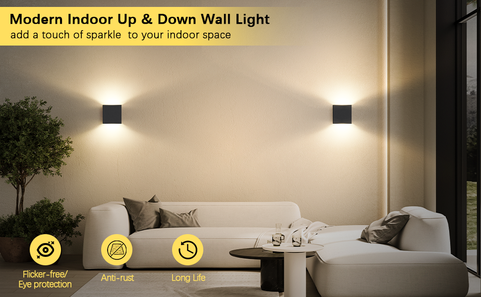 Modern indoor wall lights illuminating a living room. Two square black fixtures project warm light upward and downward on beige walls, creating ambient lighting above a white sofa.