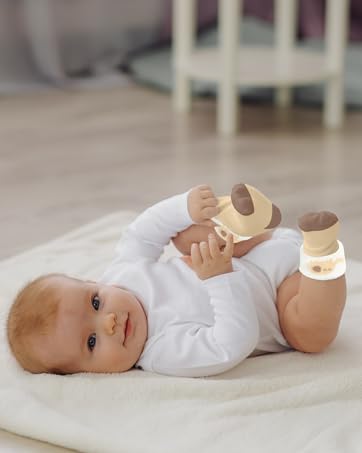 Wooden teething toy being held by an infant wearing white clothing while lying on a light-colored carpet or mat.