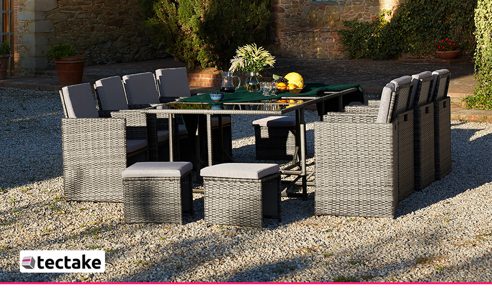 avec chaises grises tissées, table en verre et tabourets assortis. Positionné sur du gravier avec fond de jardin.