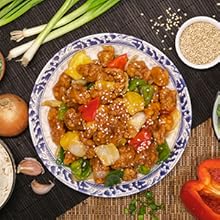 Authentic sweet and sour pork on white plate surrounded by organic vegetables and sesame seeds.