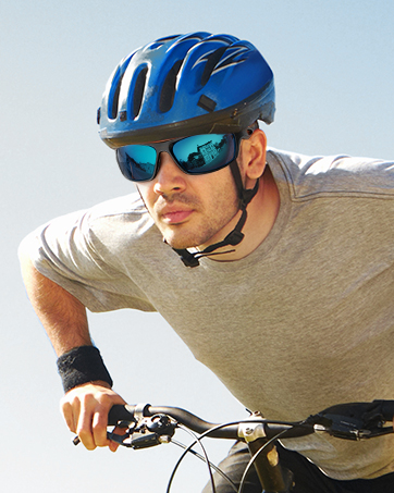Blue cycling helmet with vents worn by cyclist. Rider also wears sunglasses with blue-tinted lenses, reflecting sky. Hands gripping bicycle handlebars visible.