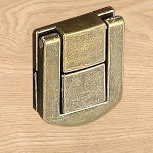 Antique brass or bronze-colored folding latch or clasp mechanism mounted on wooden surface.